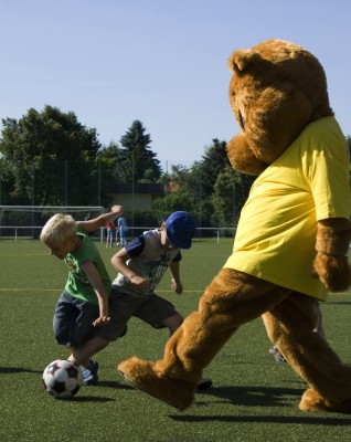 Maskottchen Paulchen spielt Fußball mit Kindern